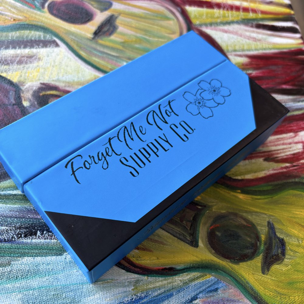 Blue Forget Me Not Supply Co. box resting on a colorful painting